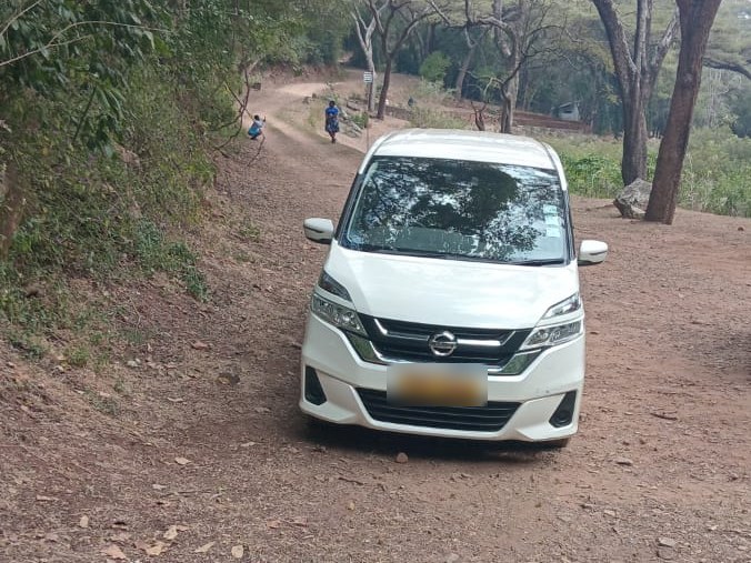 A VenMax Nissan Serena on a gravel road through the trees